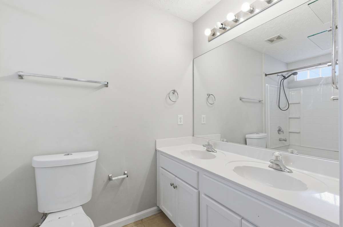 Close-up of the pristine white double vanity with a large mirror and excellent lighting.