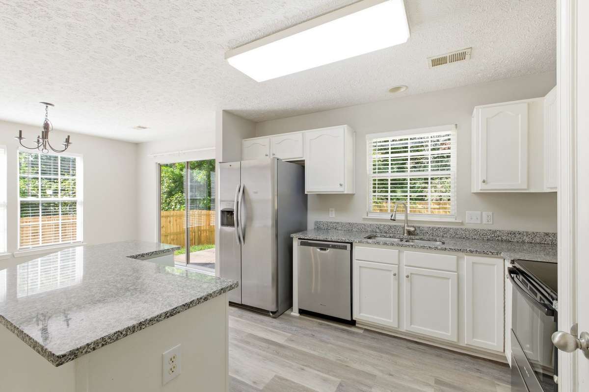 Granite kitchen featuring crisp white cabinetry and the included stainless steel refrigerator