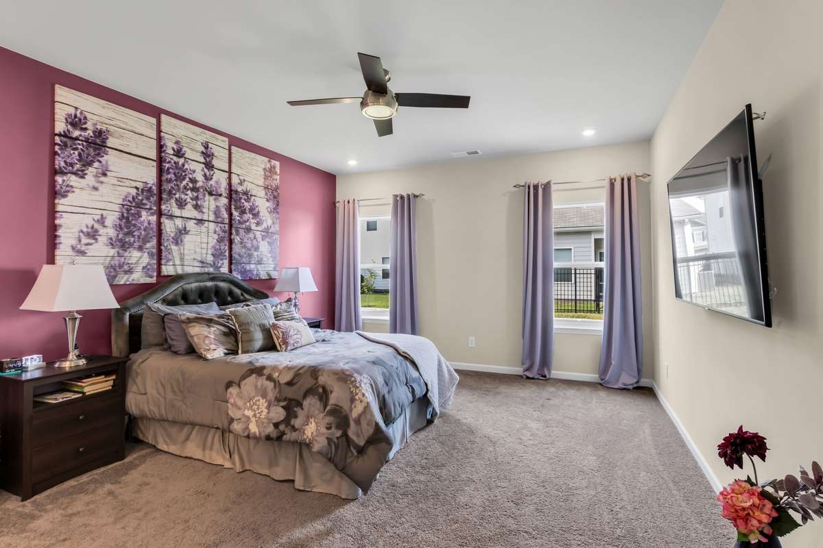 Large primary retreat features a spacious layout, elegant accent wall, ceiling fan, abundant natural light, and room for a sitting area or reading nook.