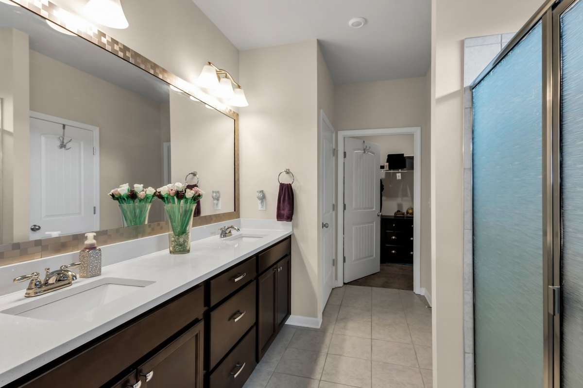 Upgraded primary bath showcases dual quartz vanities, abundant cabinet storage, oversized tiled shower, and a spacious walk-in closet.