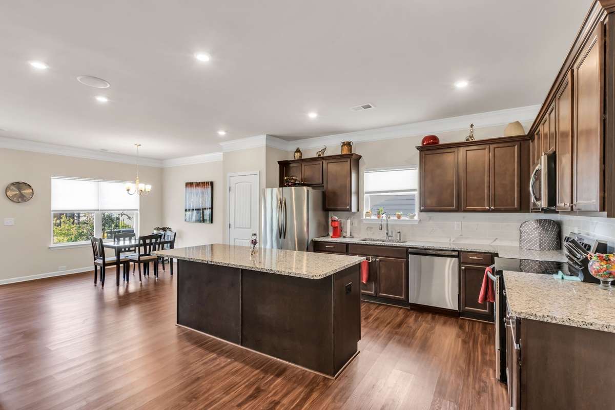 Inviting open floor plan with a gorgeous kitchen featuring a large granite island, stainless steel appliances, abundant cabinetry, tile backsplash, recessed lighting, and spacious dining area—designed for effortless everyday living and entertaining.