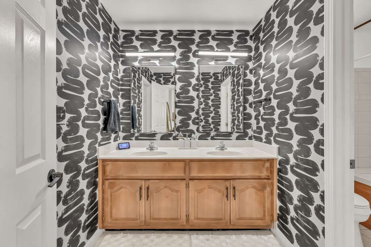 The primary bathroom with double vanities + tile floors. Seller will remove wall paper and paint if buyer prefers.