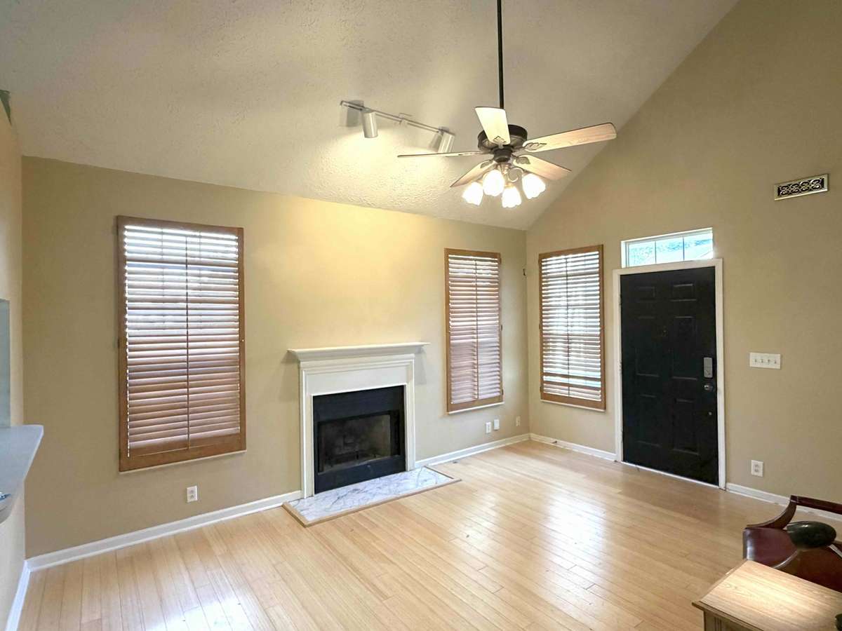 Bright and open living room with vaulted ceilings, hardwood floors, and a cozy fireplace as the focal point. Multiple windows bring in great natural light.