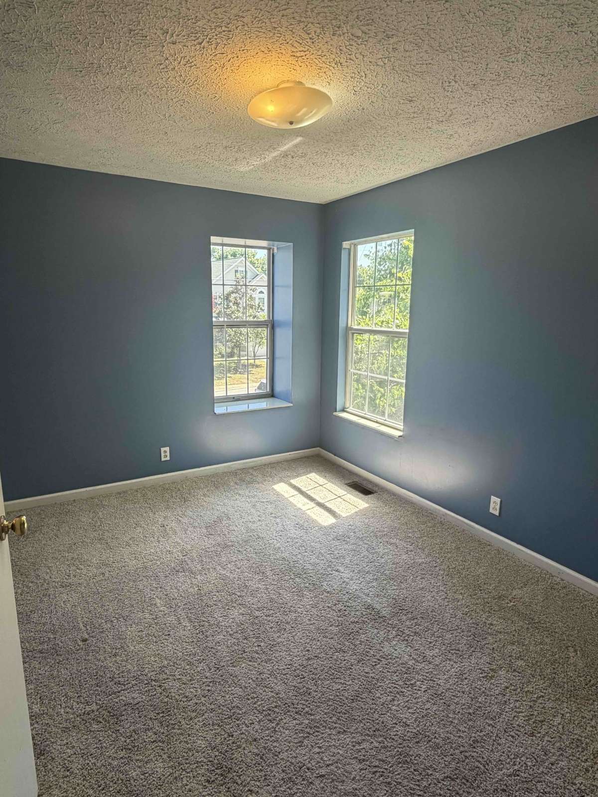 Secondary bedroom with soft natural light, neutral carpet, and two windows creating a bright, comfortable space.