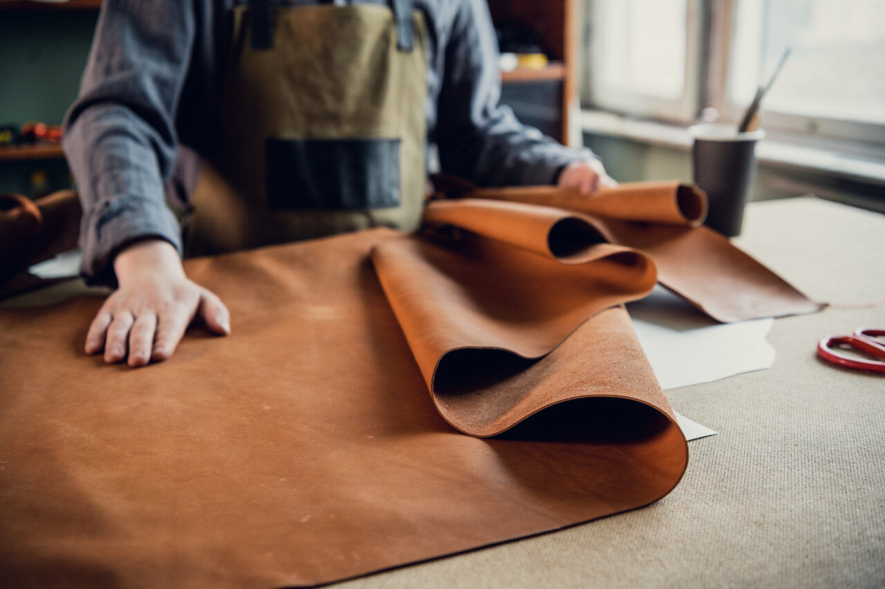 A young apprentice in a shoe workshop preparing leather for further use on a large table.