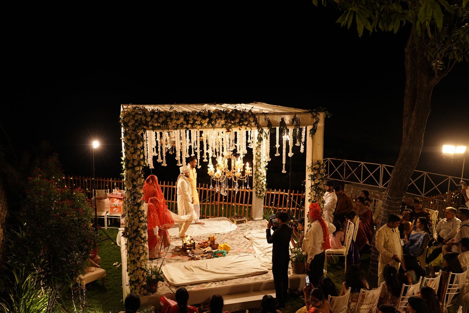 A candle-lit mandap glowing in a garden at night