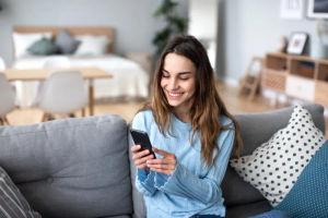 Money Comes From Within 8 Girl holding phone sitting on the couch with her bed in the background.