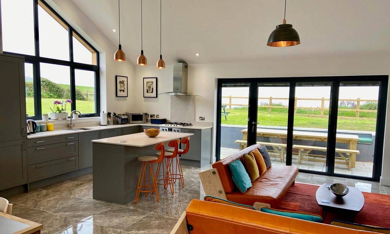 Open plan neutral style kitchen against vibrant living room with 3 pewter cone pendants above kitchen island