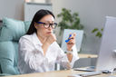 A young Asian woman with glasses uses an inhaler to help with asthma