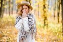 A blonde woman wearing a hat and blowing her nose in an autumn background