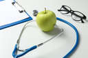 A stethoscope and an apple on white background representing health
