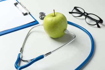 A stethoscope and an apple on white background representing health