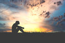A silhouette of a person sitting with their heads down in sorrow in the meadows