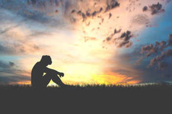 A silhouette of a person sitting with their heads down in sorrow in the meadows
