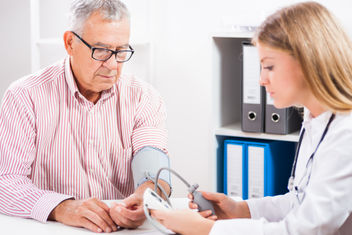 A female doctor checking an older male patient blood pressure in the office