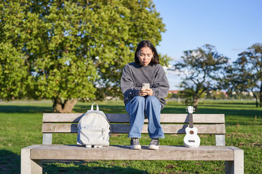 Girl sitting on park bench looking at phone
