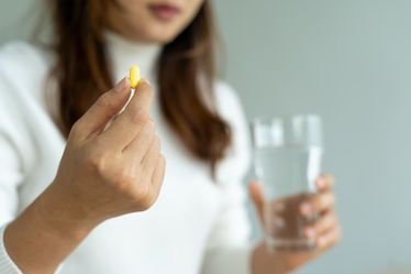 Woman holding a pill in one hand and glass of water in the other