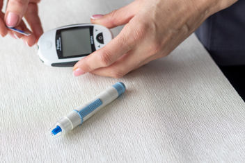 Close up shot of a person using the glucometer instrument on the white surface