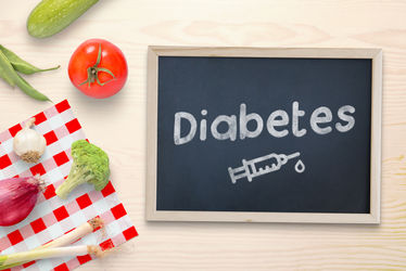 Diabetes written on a chalkboard with a drawing of an insulin injection, in addition to healthy food, vegetables