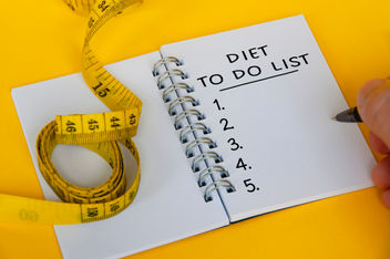Diet plan text on white notepad with measuring tape on yellow background