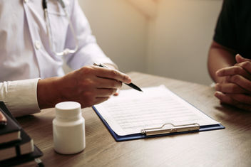 A physicians hand holding a pen and talking to the patient about medication and treatment