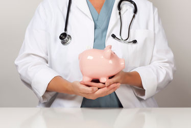 Physician in a white coat with a stethoscope holding piggy bank