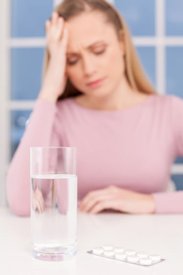 A depressed young woman holding her head while glass of water and medicines laying on foreground