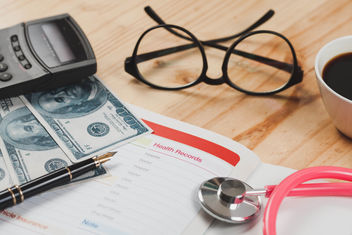 Health records in book note with fountain pen, eyeglasses, and money on a wooden background