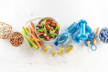 Healthy fresh salad with tomatoes surrounded with exercise equipment and measuring tape