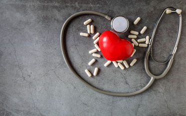 Heart with stethoscope and pills on gray background