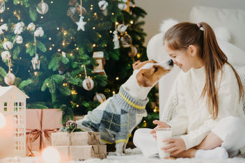 Chica con perro al lado del árbol de Navidad