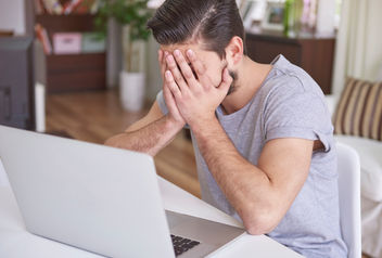 Hombre con la cabeza entre las manos frente a la computadora