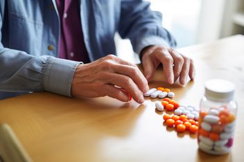 Persona vertiendo pastillas de un frasco sobre una mesa