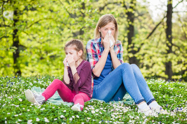 Mother and daughter together outdoors and blowing their nose as a result of allergies