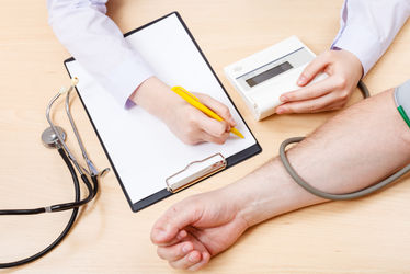 Nurse measuring a patients blood pressure and documenting the results on paper