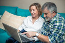 A retired couple sitting on sofa and looking at their laptop screen
