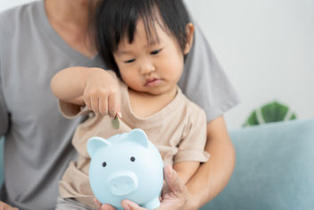 A young child putting a coin into piggy bank for savings