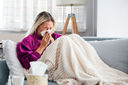 A blonde haired woman blowing her nose with a tissue because of a common cold