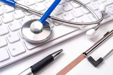 Stethoscope on computer keyboard on white background with pens