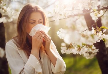 Woman blowing her nose with a flowering tree in the background