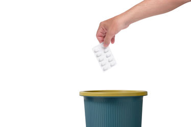 A hand throwing package pills in trash