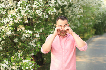 A man wiping his watery eyes standing next to flowers