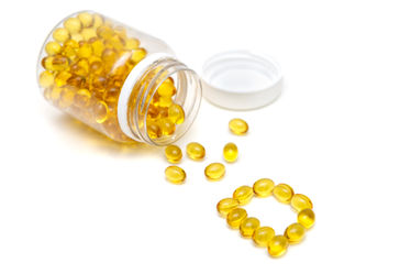 Vitamin D medication bottle and yellow pills spilled on white background