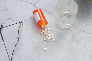 Pastillas blancas sobre una mesa con un vaso de agua y gafas.