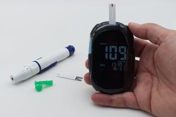 A woman with diabetes using glucometer, lancet pen and test strip on background