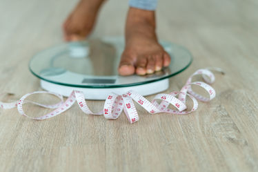 Person stepping on scale with tape measure on the floor