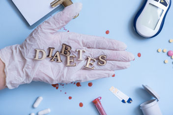 The word Diabetes on physicians gloved hand with medical instrument on blue background