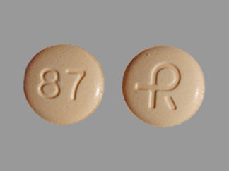 Esto es un Tableta Er 24 Hr imprimido con R en la parte delantera, 87 en la parte posterior, y es fabricado por None.