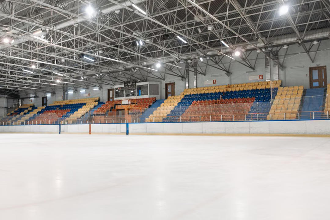 Empty modern ice hockey rink with colored seating and industrial ceiling.
