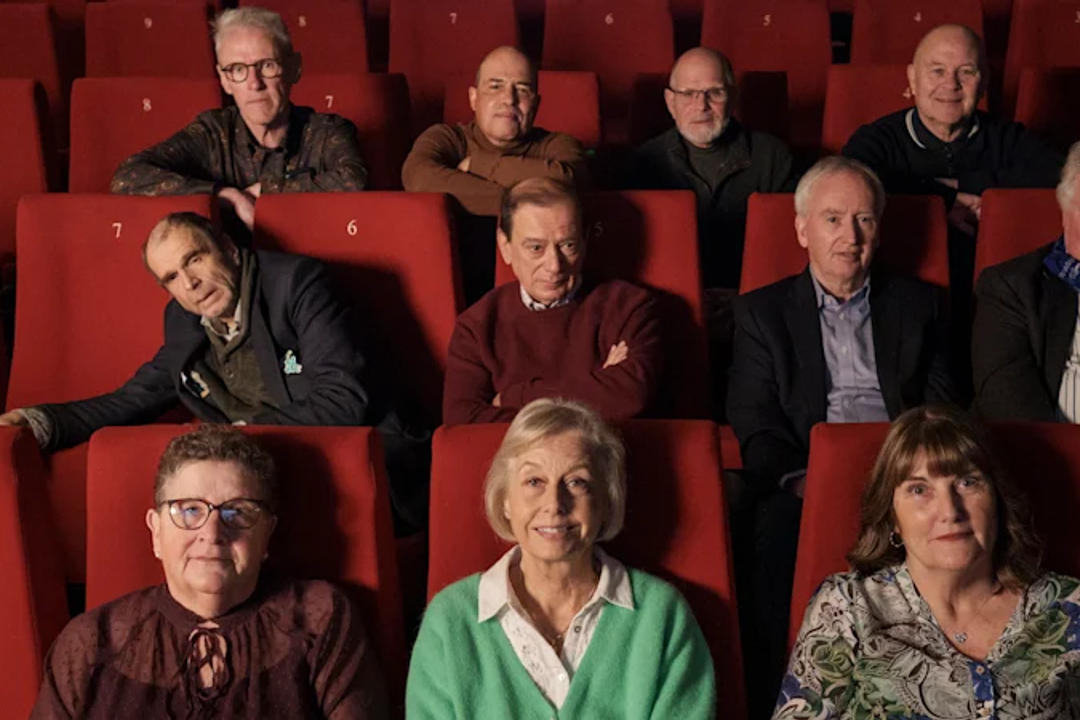Nine people seated in red movie theater chairs arranged in rows